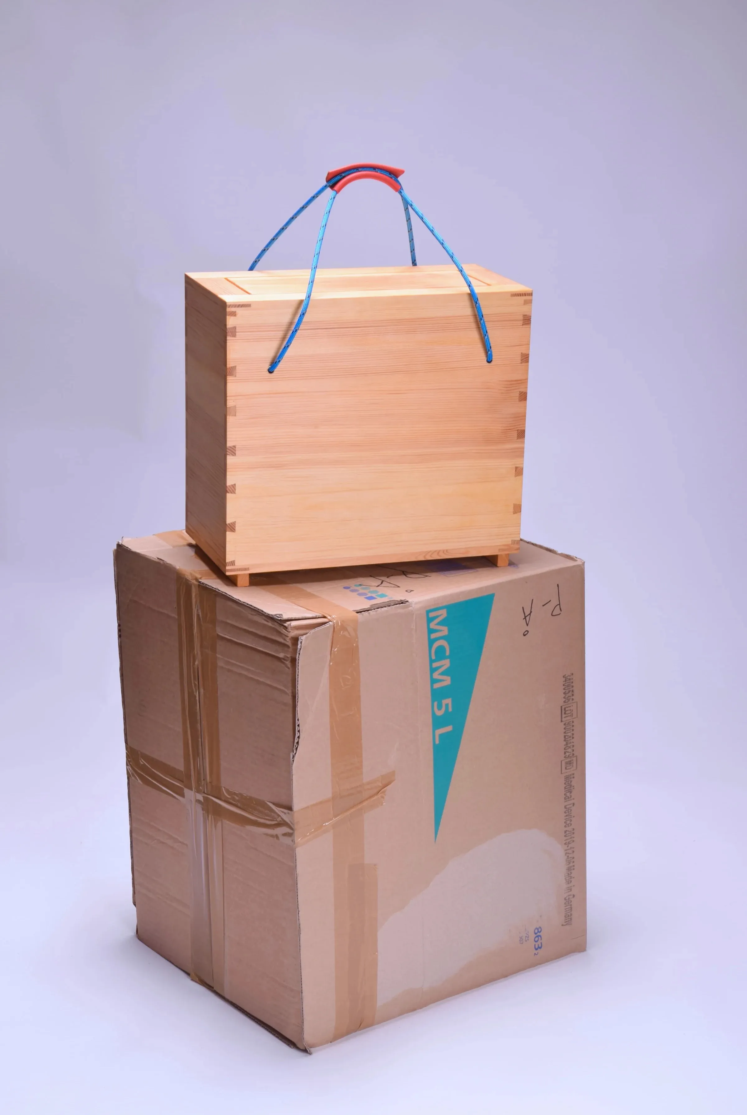 Wood box with blue stripes standing on top of a cardboard box